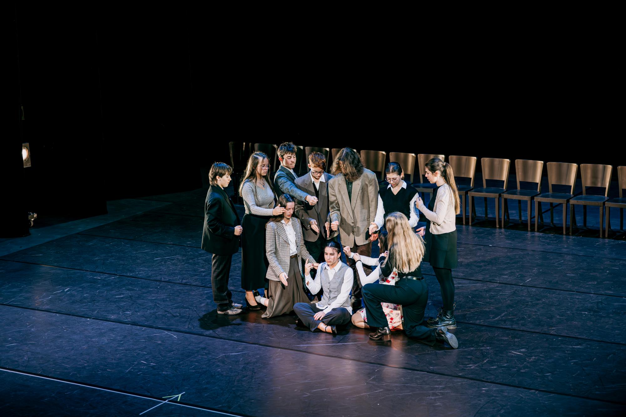 Eine Person sitzt auf dem Boden um sie herum stehen und hocken weitere Personen, die ihre Arme ausstrecken. 