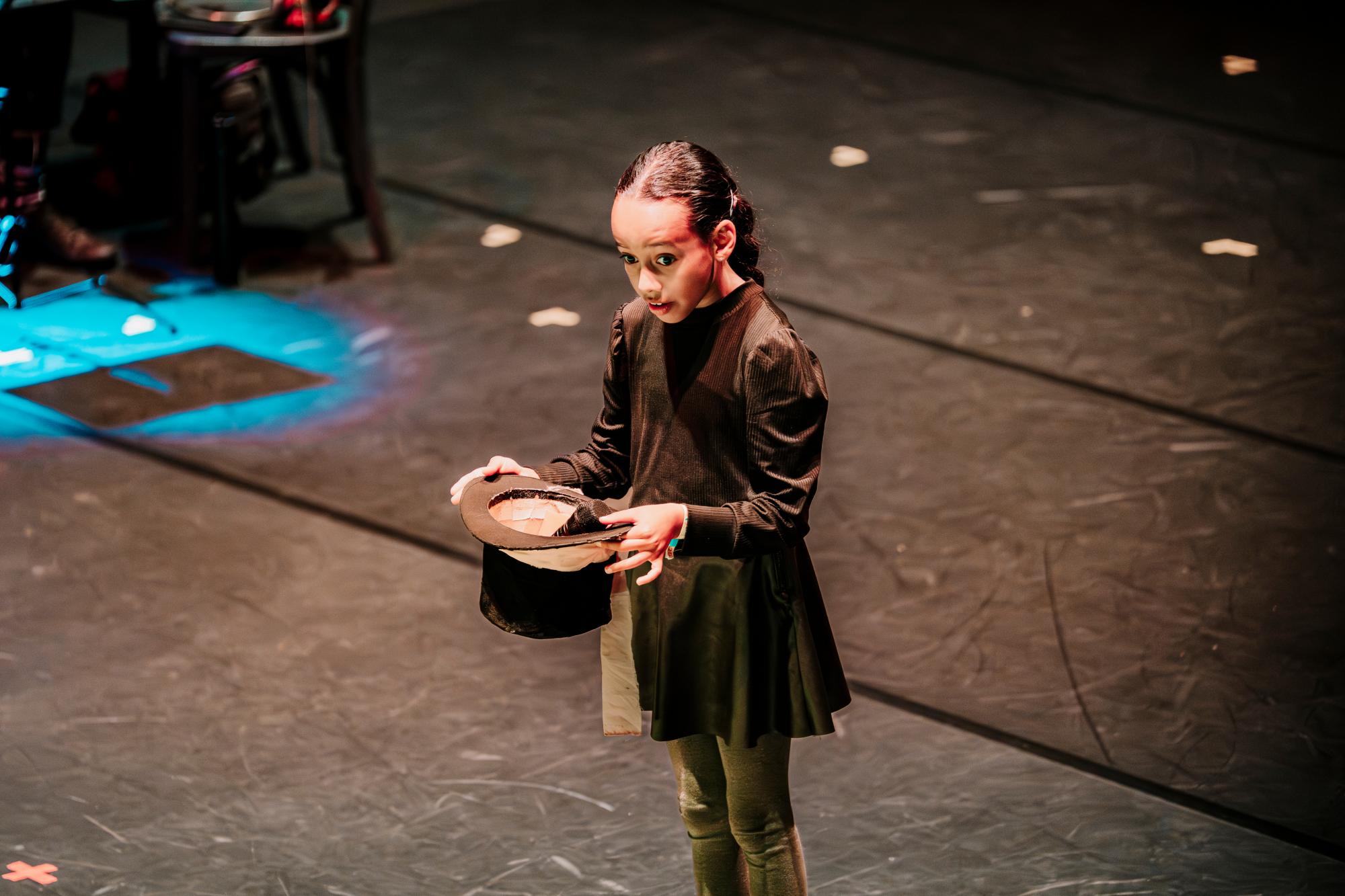 Ein Mädchen hält einen schwarzen Zylinder verkehrt herum in der Hand.