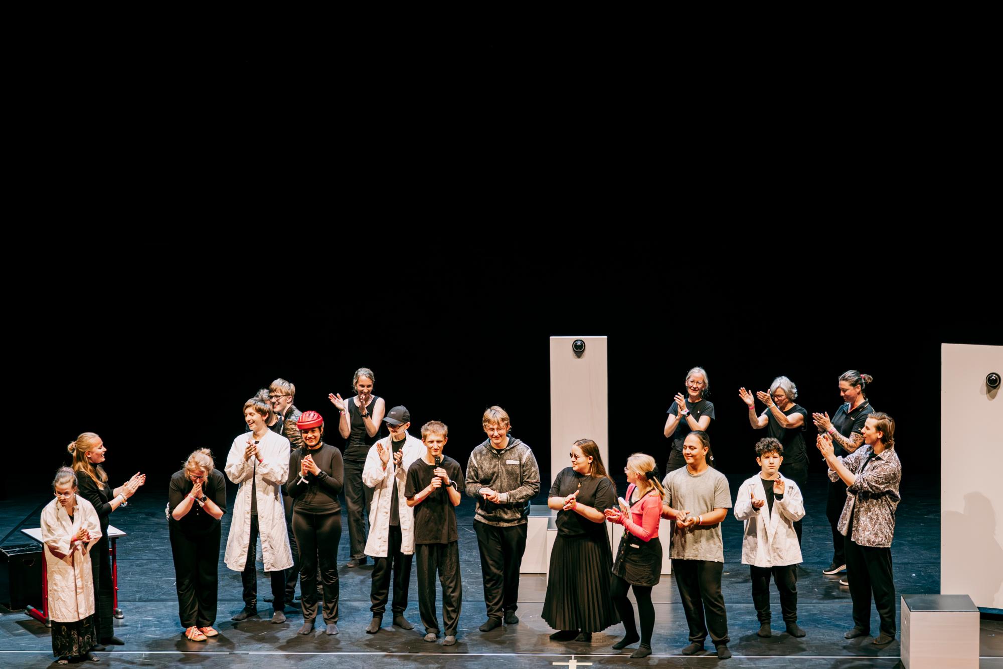 Das Ensemble steht mit der Spielleitung auf der Bühne und klatschen.